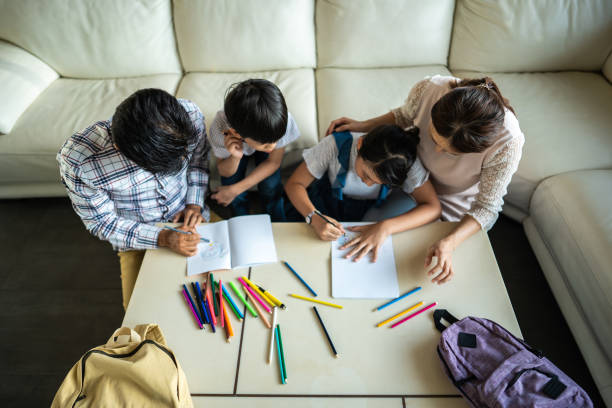 High angle view of Taiwanese family with two children sitting in living room, drawing and coloring together and having good time